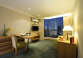 A hotel room with a desk, chair, TV, and a view of the cityscape at night.