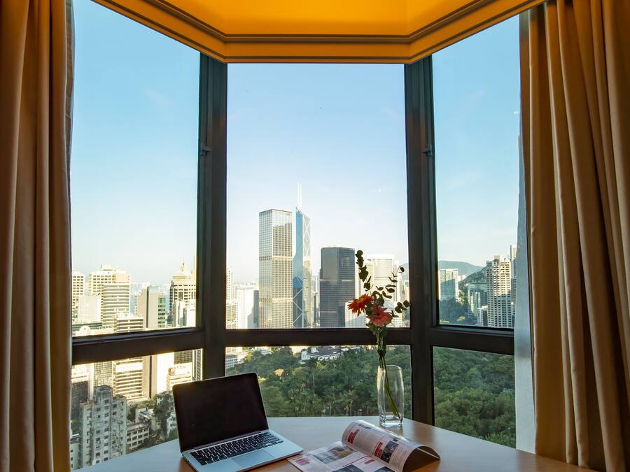 A room with a large window, a laptop, a vase with flowers, and a newspaper on a table.