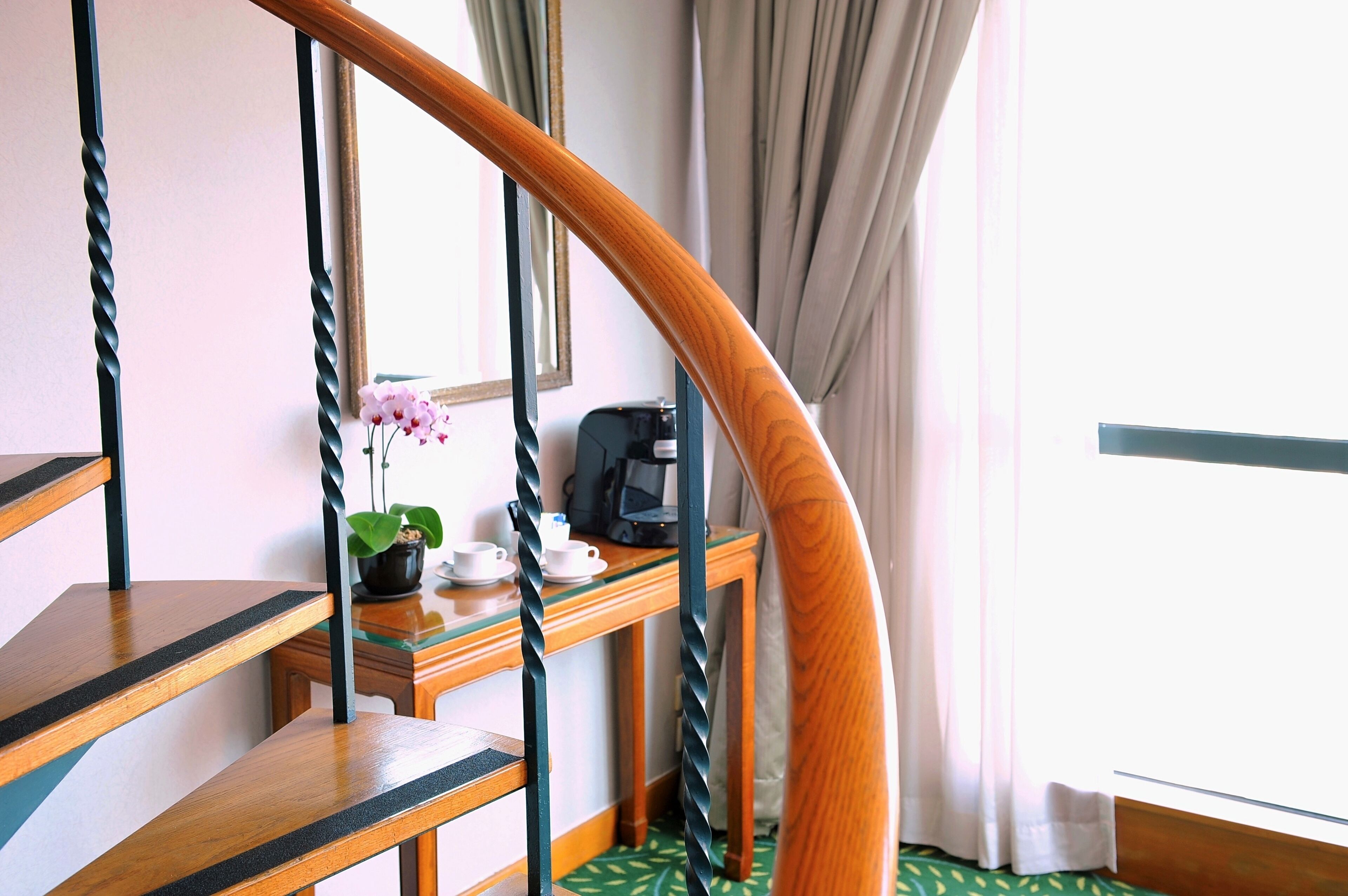 A staircase with a wooden handrail and a desk with a coffee machine, cups, and a potted plant.
