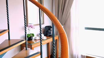 A staircase with a wooden handrail and a desk with a coffee machine, cups, and a potted plant.