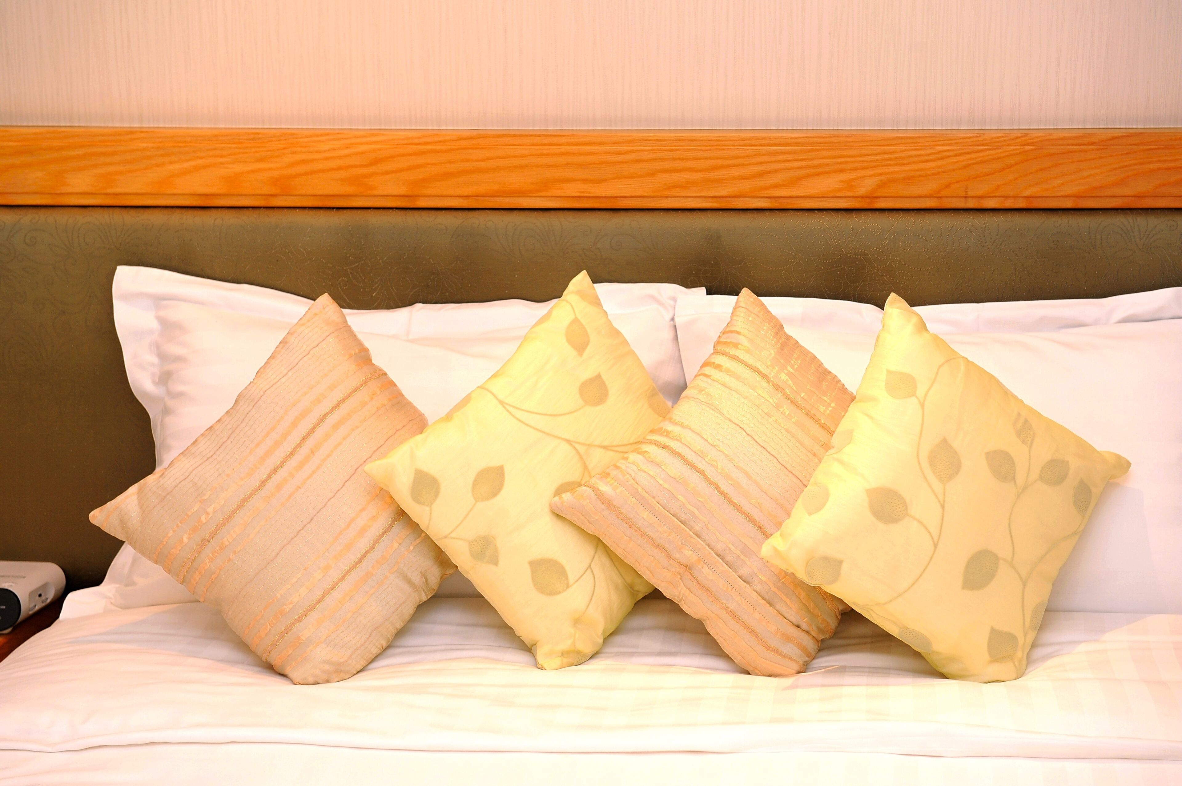 Un lit avec une tête de lit en bois et quatre oreillers ornés de motifs de feuilles.