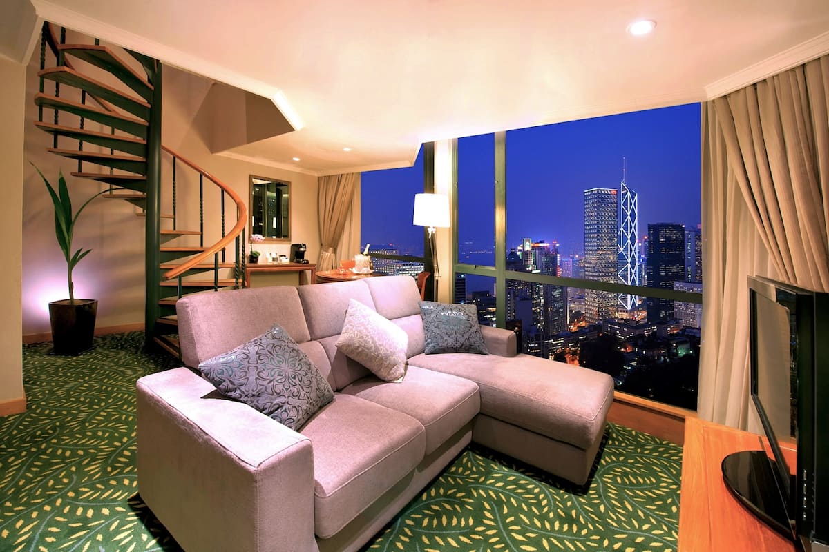 A modern living room with a curved staircase, a sofa with patterned cushions, and a large window offering a cityscape view.
