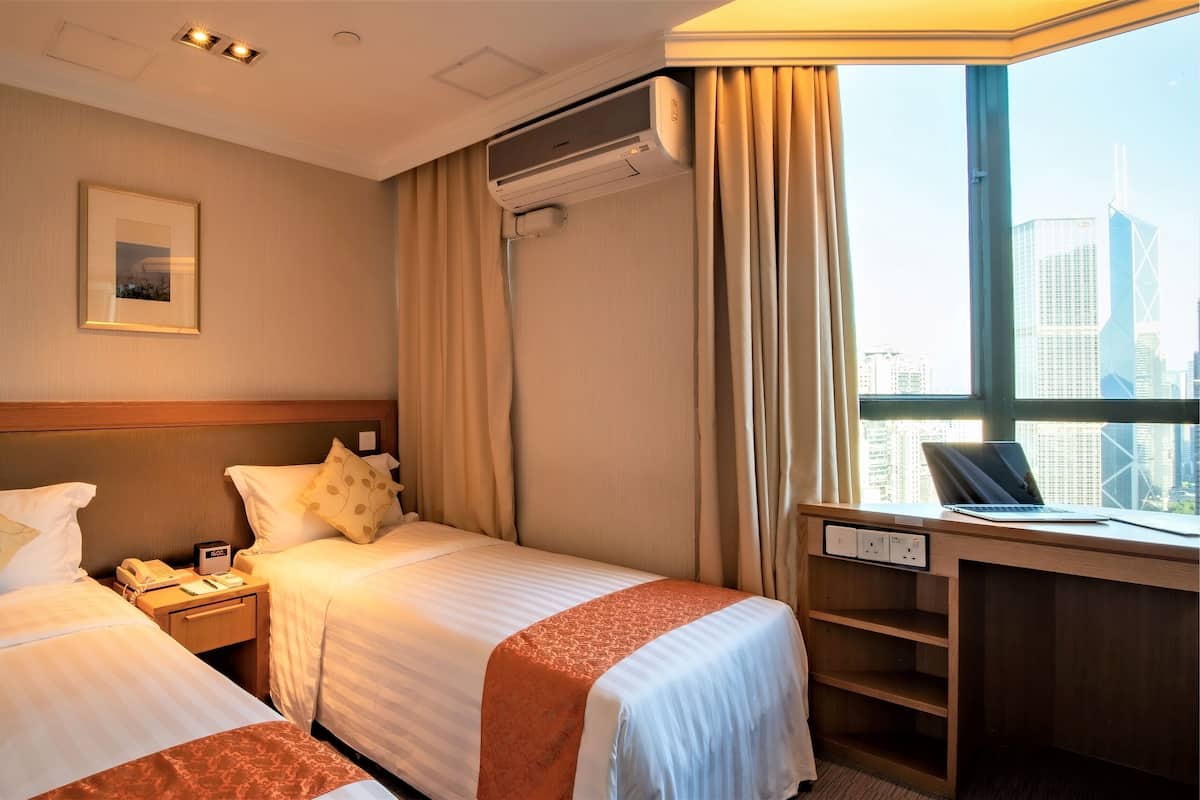 A hotel room with two beds, a desk with a laptop, an air conditioning unit, and a city view.