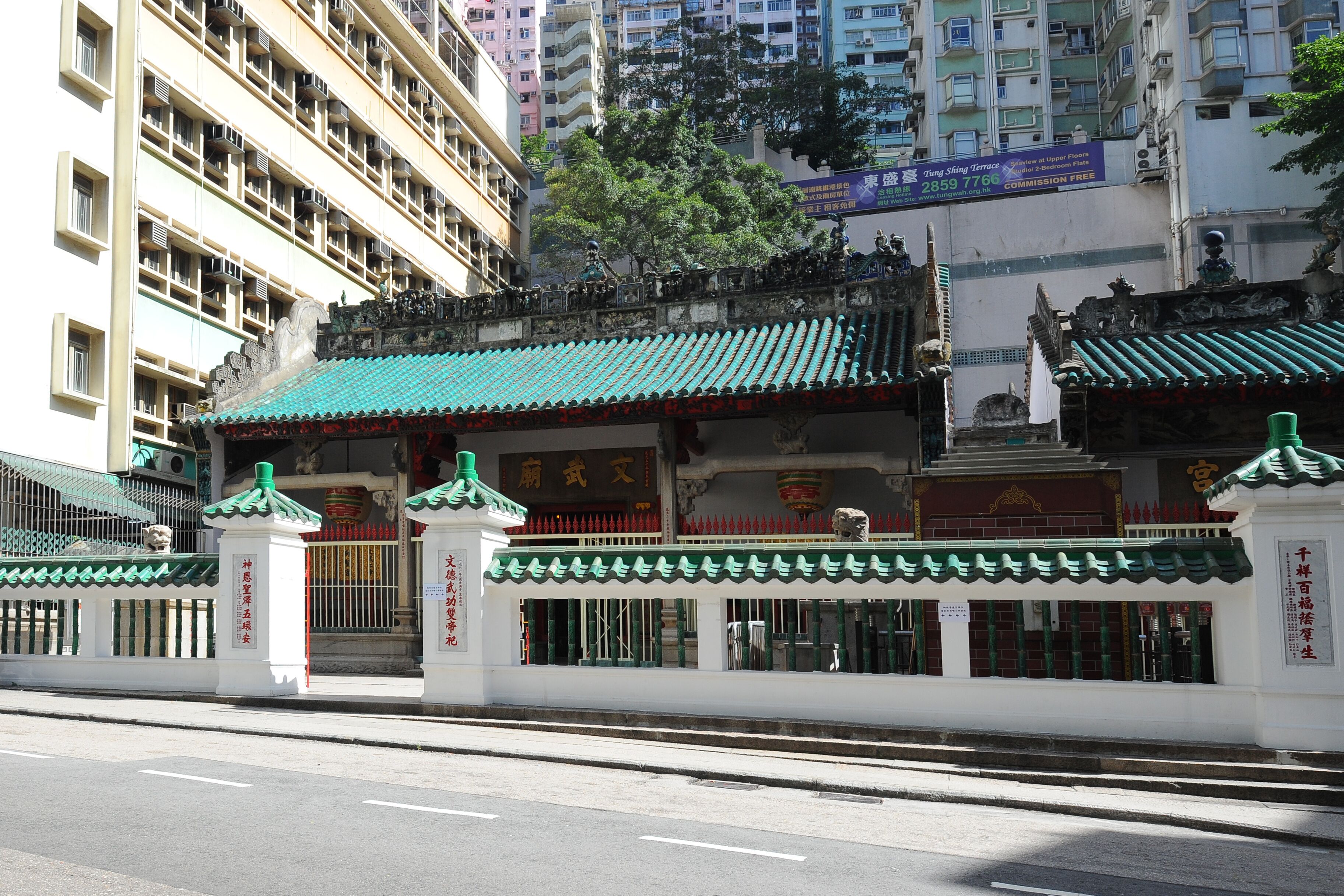 A traditional Chinese building with a green roof and white walls, featuring a gate and a statue.