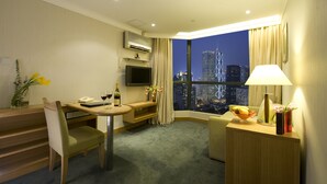 Une chambre d’hôtel comprenant un coin repas, une télévision, un bureau, une lampe et une vue sur le paysage urbain la nuit.