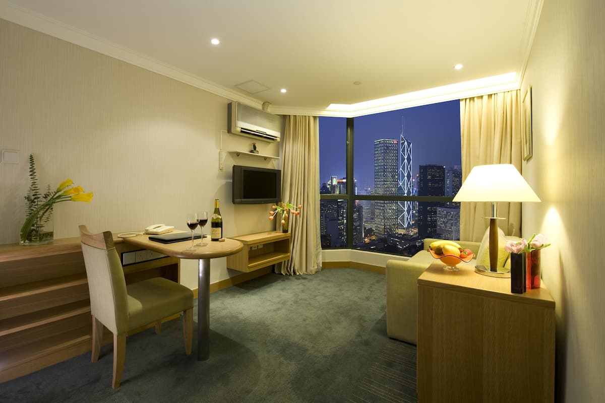 A hotel room with a dining area, a TV, a desk, a lamp, and a view of the cityscape at night.