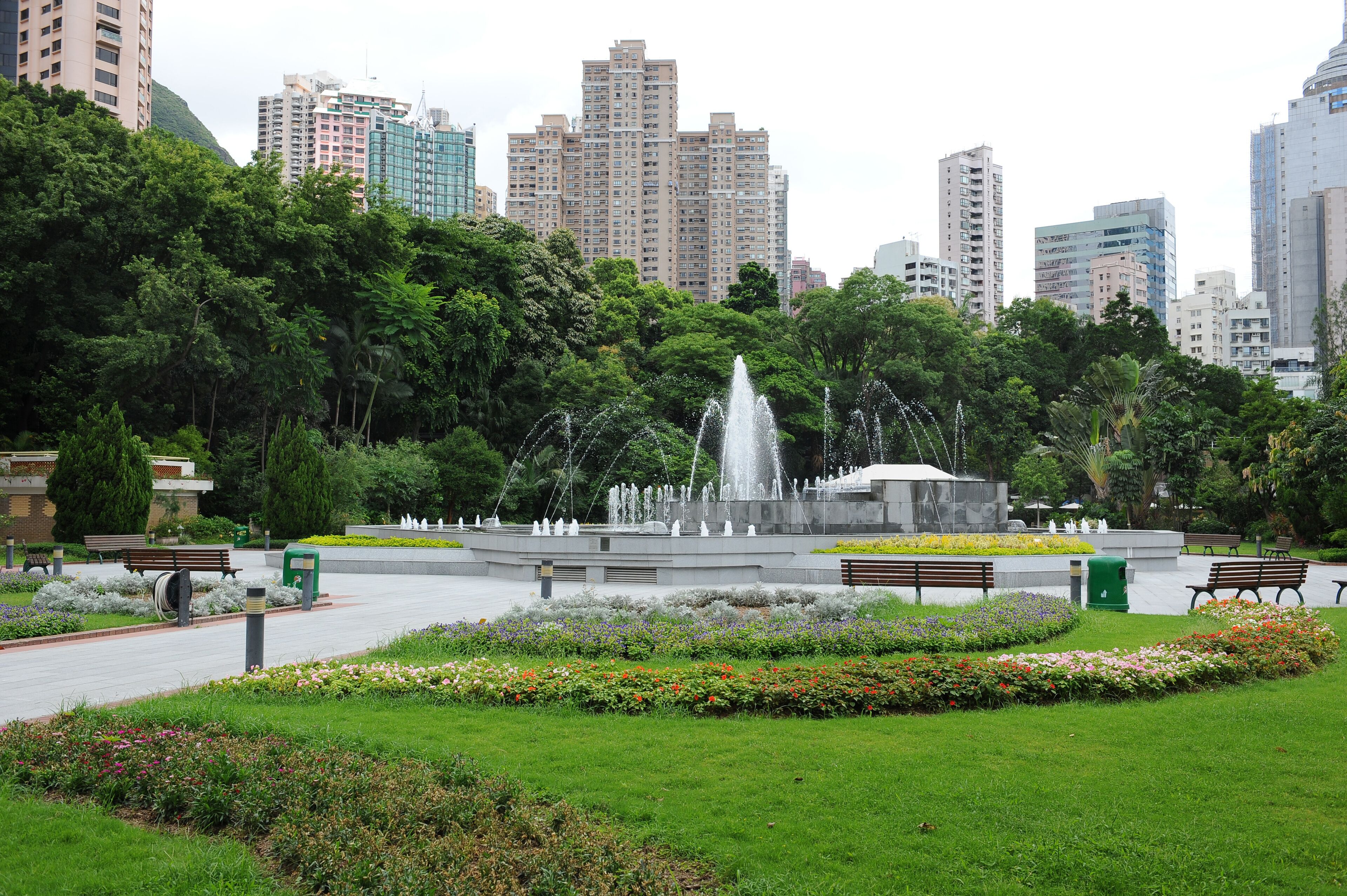 Un parque con una fuente, bancos y un paisaje urbano al fondo.