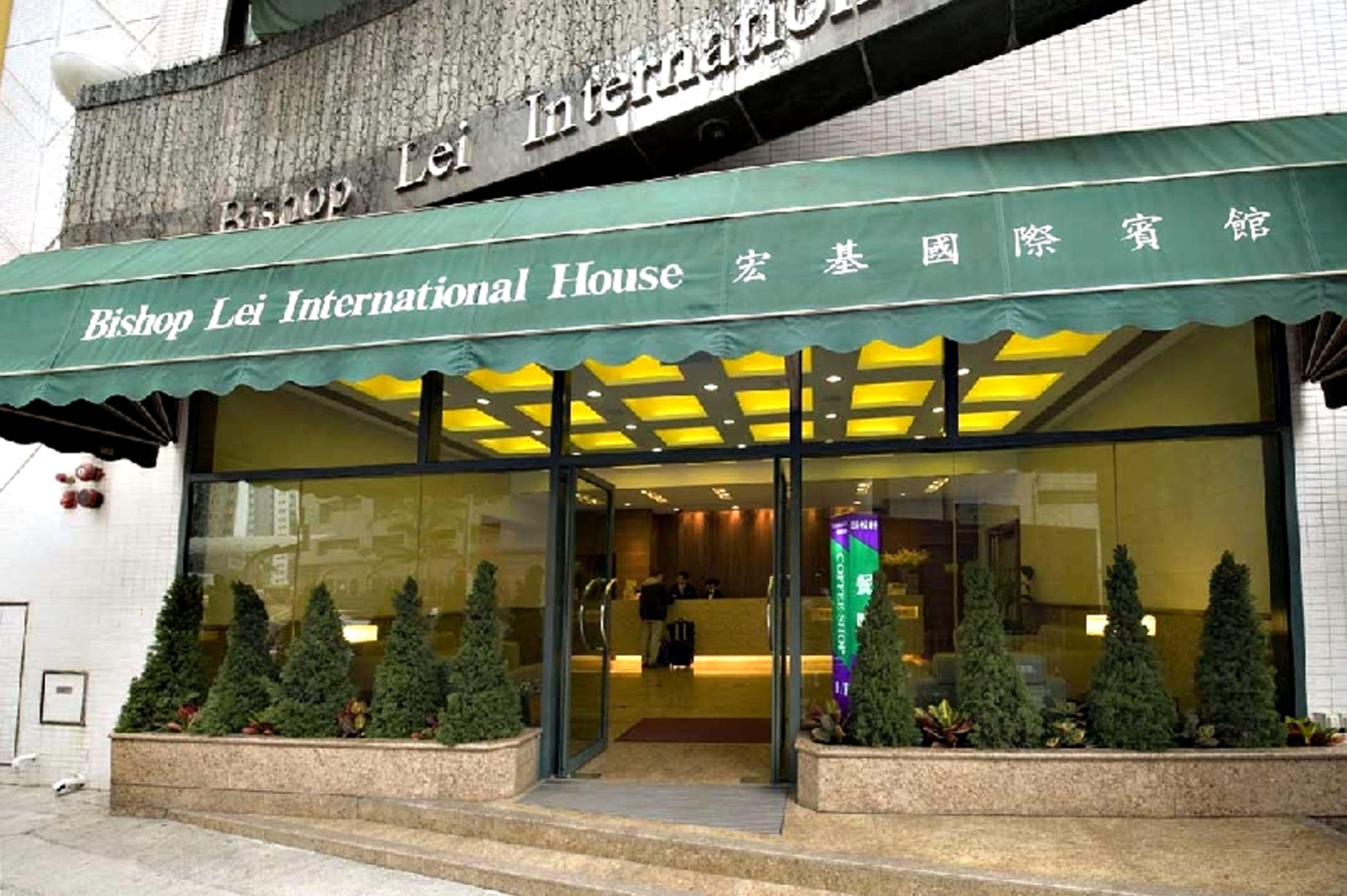 El exterior del Bishop Lei International House con un toldo verde y una entrada de cristal.