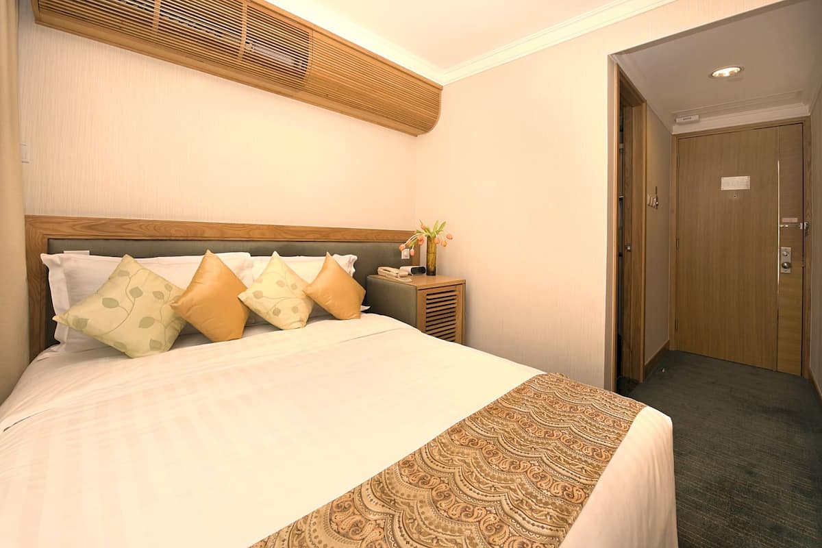 A hotel room with a large bed, a bedside table with a vase of flowers, and a wooden door.