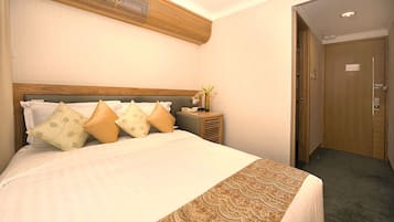 A hotel room with a large bed, a bedside table with a vase of flowers, and a wooden door.