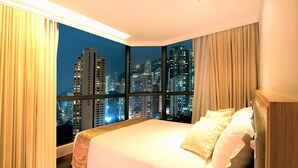 Une chambre d’hôtel dotée d’une grande fenêtre donnant sur la ville, avec une vue particulièrement agréable la nuit.