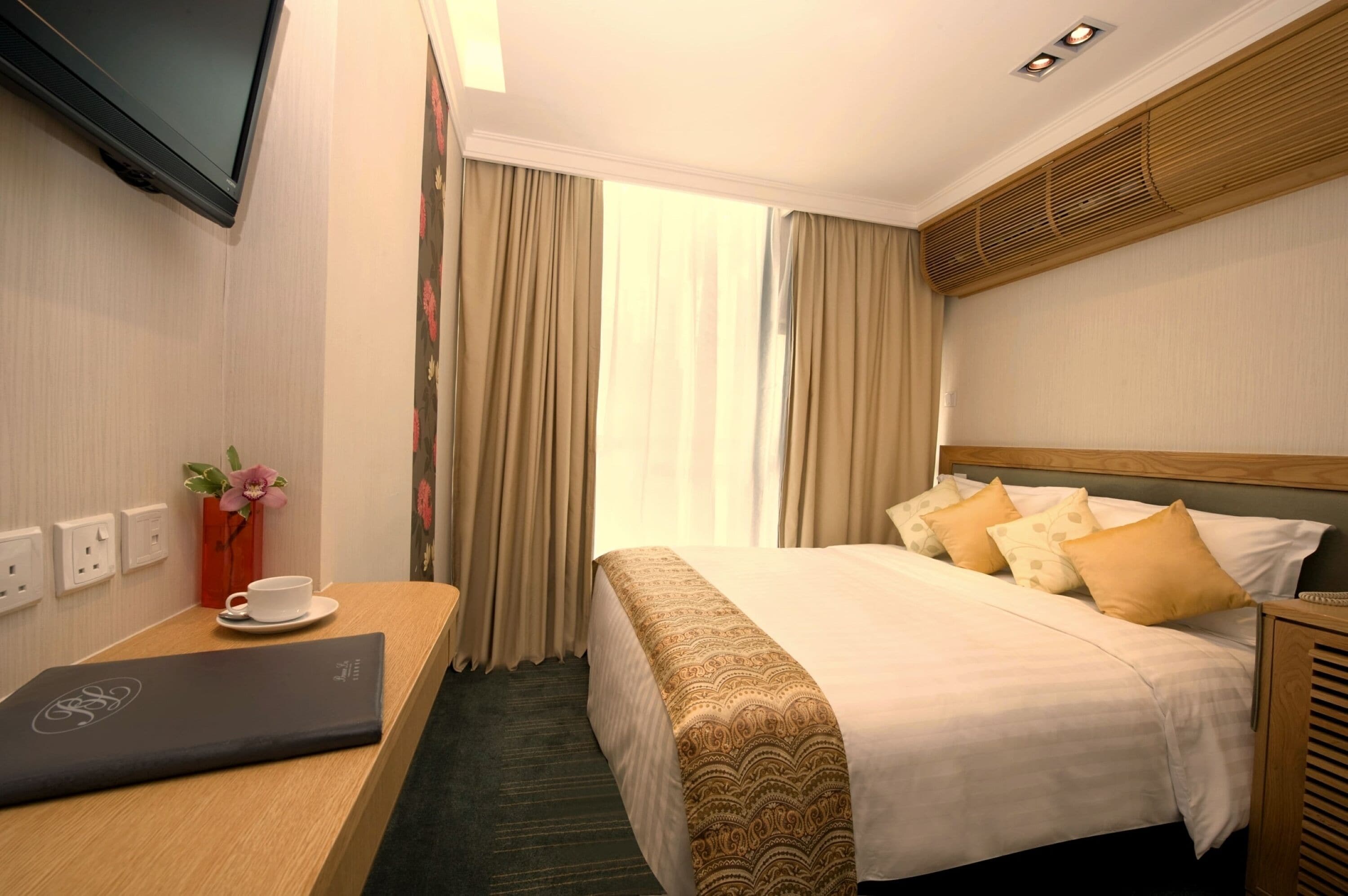 A hotel room with a bed, a desk with a laptop, a TV, and a window with curtains.