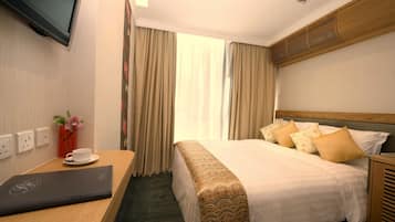 A hotel room with a bed, a desk with a laptop, a TV, and a window with curtains.