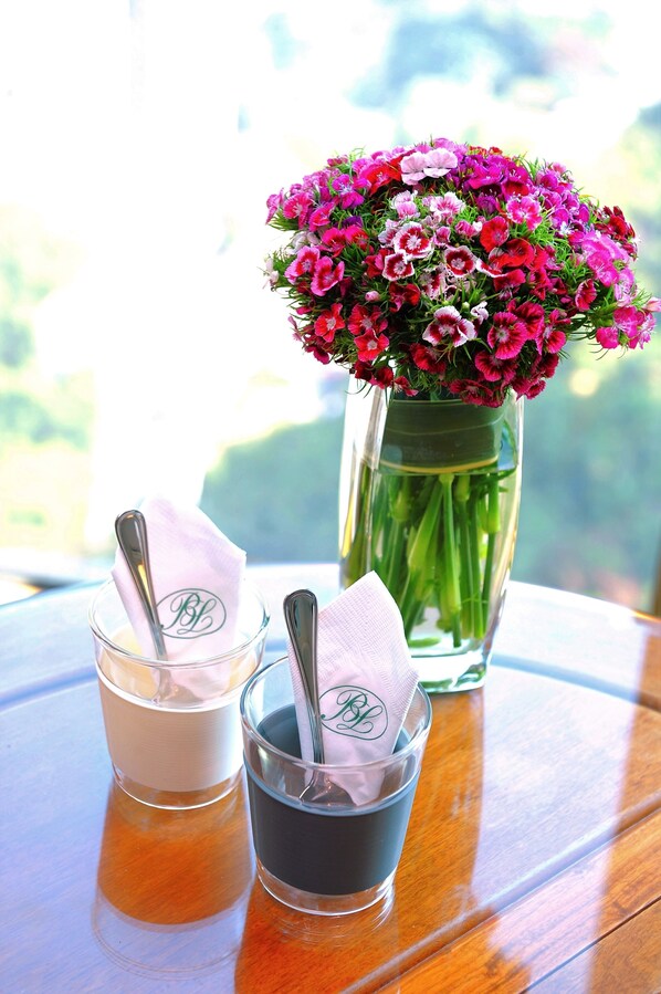 Two glasses of iced tea with napkins on a wooden table, a vase with pink flowers, and a window in the background.