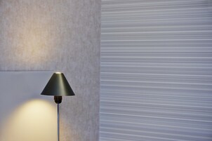 Uma luminária moderna com base metálica e cúpula preta, posicionada em frente a uma parede texturizada com padrão discreto.