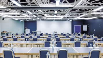 Ein Konferenzraum mit Reihen von Tischen und Stühlen, einer Projektionsleinwand und einem Rednerpult.