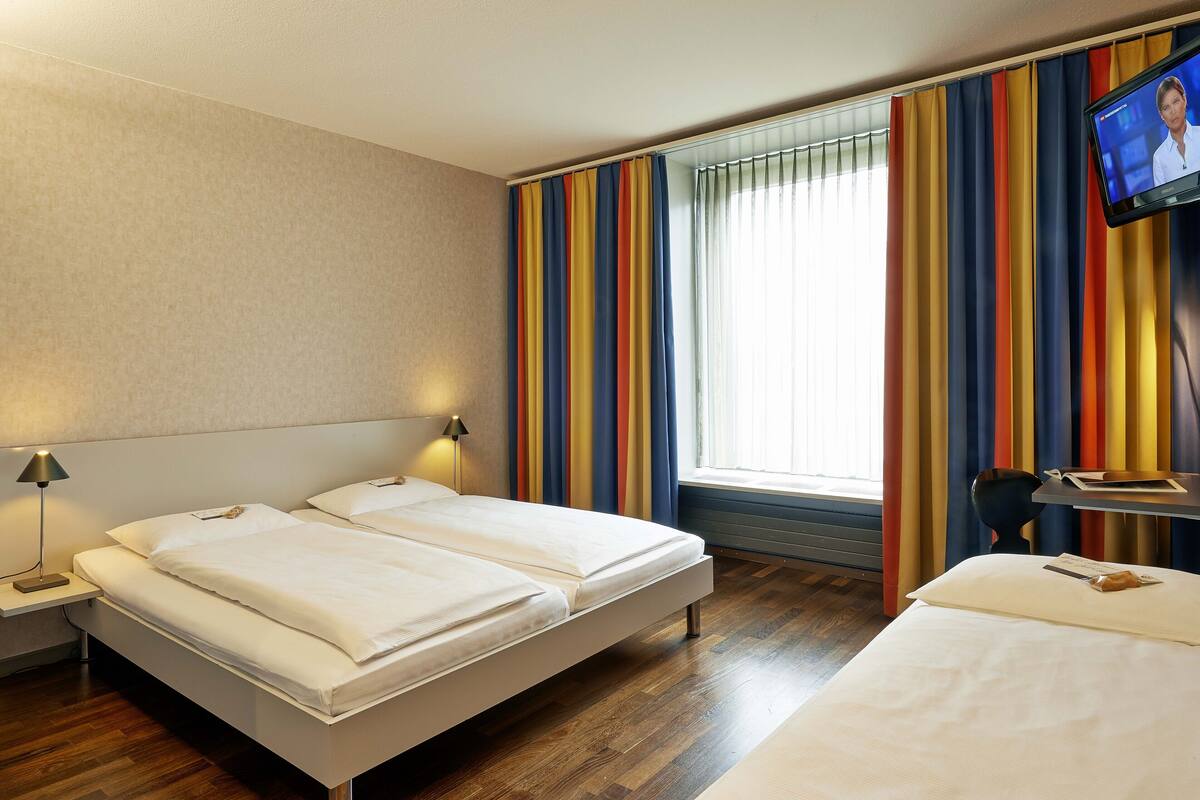 Habitación de hotel con dos camas, un televisor y una ventana con cortinas a rayas.