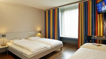 A hotel room with two beds, a TV, and a window with striped curtains.