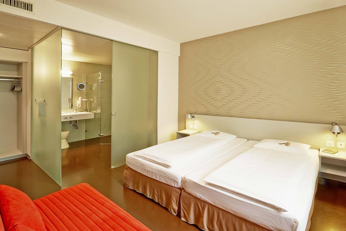 Habitación de hotel con dos camas, un baño y una silla roja.