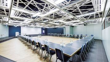 Un salón de conferencias con una larga mesa, sillas y un techo alto con diseño geométrico.