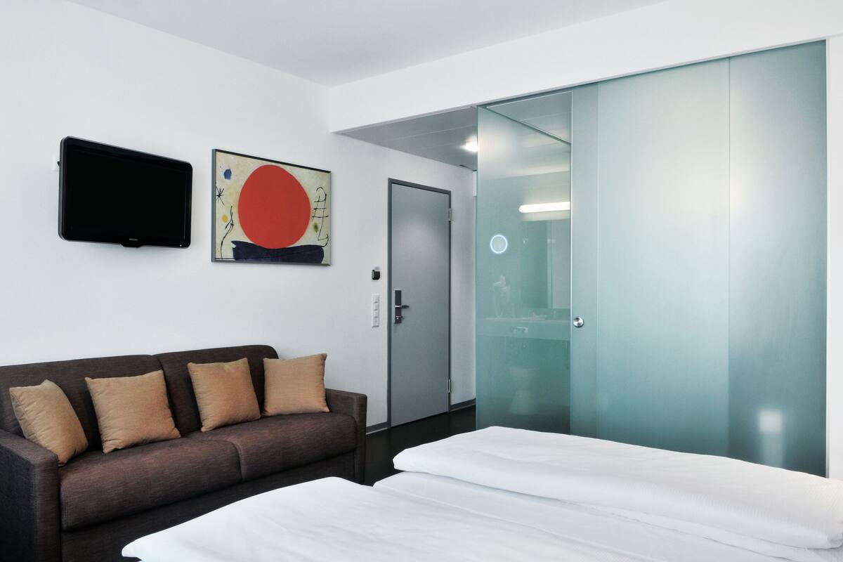 Una habitación de hotel moderna con una cama, un sofá, un televisor de pantalla plana y una puerta de vidrio.