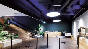 Un espacio interior moderno con una escalera, varias mesas con bebidas y una zona de recepción.