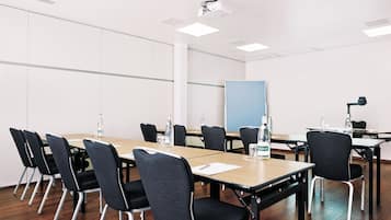 Un salón de conferencias con una larga mesa, sillas, un proyector y una pizarra.