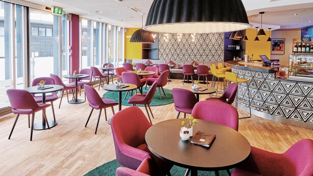 Un moderno vestíbulo de hotel con mesas y sillas redondas, una zona de bar y una pared con diseño.