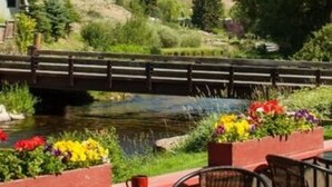 An outdoor seating area with a view of a river and a bridge, surrounded by greenery and flowers. - Inn on the Creek (Jackson)