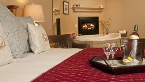 A hotel room with a bed, a fireplace, a bathtub, and a tray with glasses and a bottle. - Inn on the Creek (Jackson)