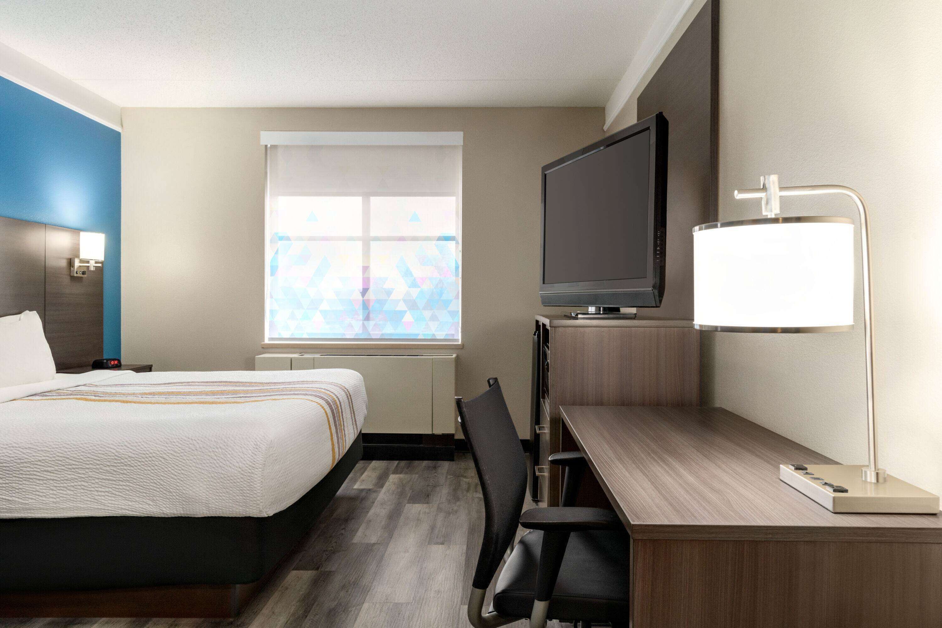 Ein Hotelzimmer mit Bett, Schreibtisch mit Stuhl, Fernseher und Lampe.