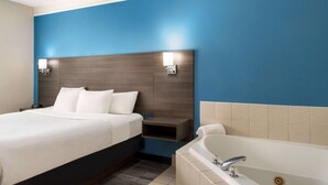 A modern hotel room with a large bed, a separate bathroom with a bathtub, and a blue accent wall.