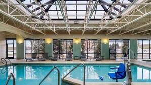 An indoor swimming pool with clear glass ceilings, lounge chairs, and a view of the outdoors.
