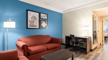Habitación de hotel con pared azul, un sofá rojo, un escritorio con una silla y una mesita.