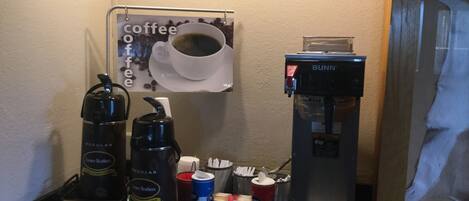 Una estación de café con una cafetera, un dispensador de agua y una taza de café sobre una encimera.