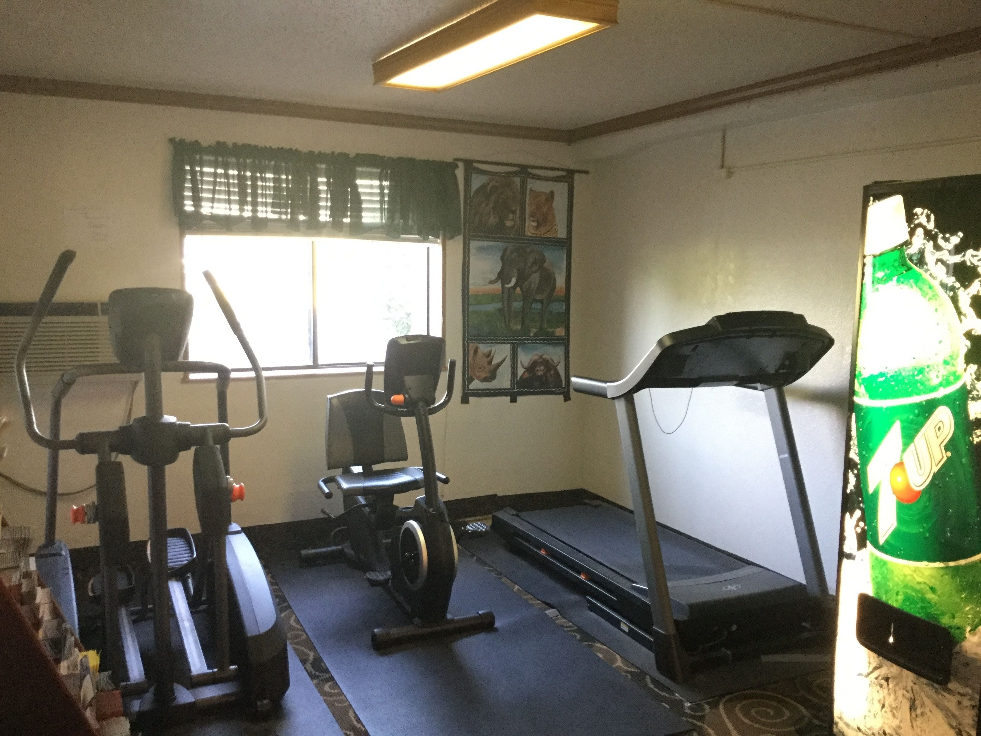 A gym with exercise equipment including treadmills and stationary bikes, a window with blinds, and a poster on the wall.