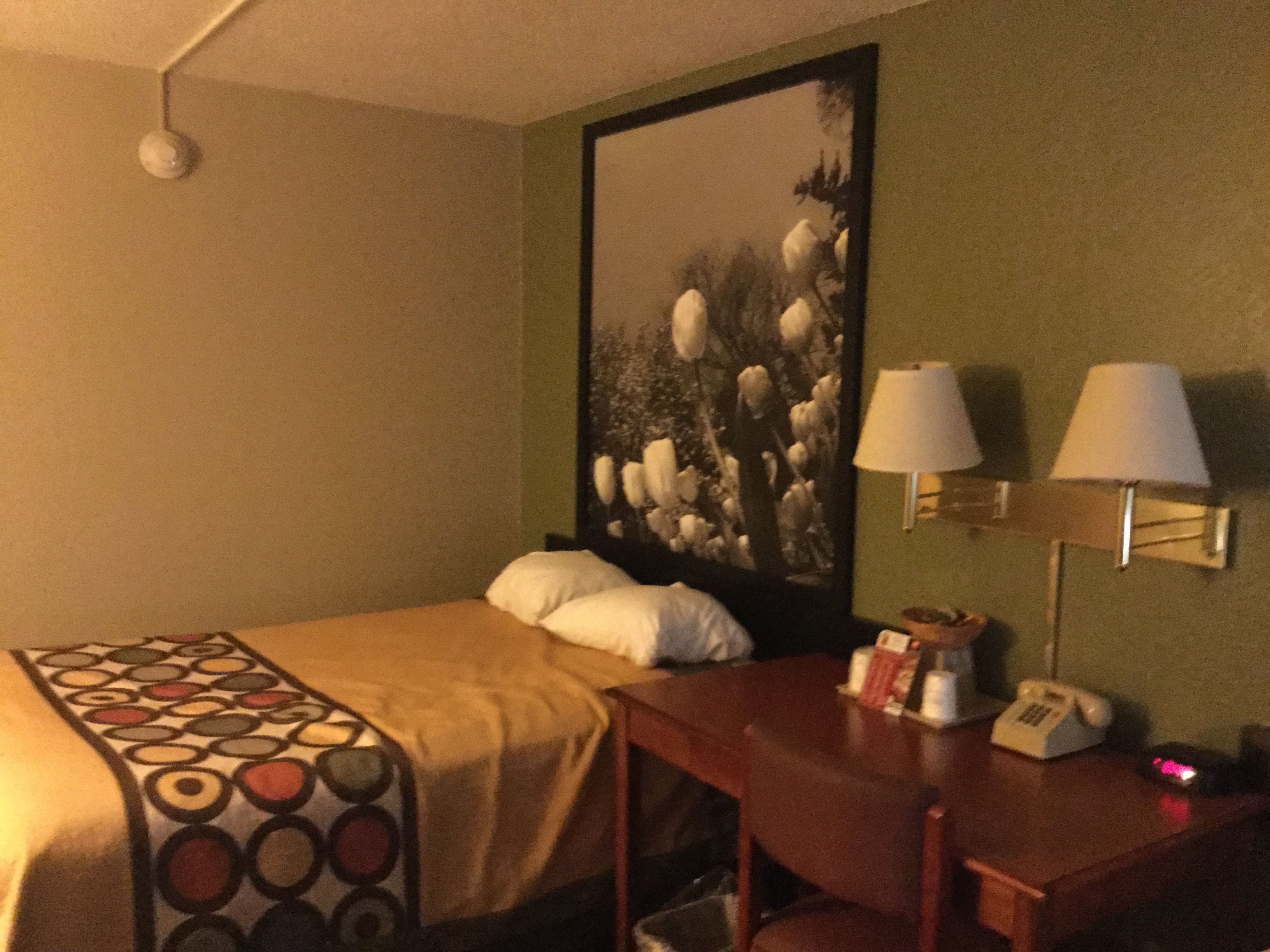 Habitación de hotel con cama, escritorio y teléfono, y una lámpara de pared.