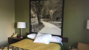 Una habitación de hotel con una cama, una mesita de noche, una lámpara, una silla y un cuadro grande en la pared.