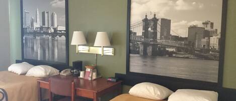 Habitación de hotel con dos camas, un escritorio y dos lámparas. Hay dos cuadros grandes en las paredes, uno con una vista urbana y otro con un puente.