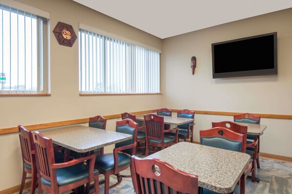 A dining area with multiple tables and chairs, a clock, and a television on the wall.