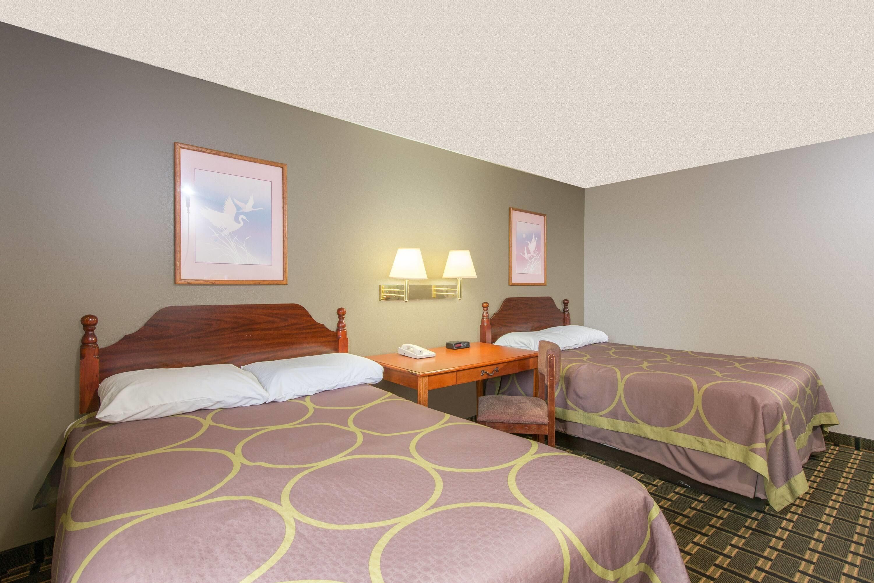 Quarto de hotel com duas camas, uma mesa com telefone, duas luminárias fixadas na parede e quadros decorativos.