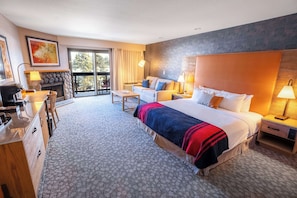 A hotel room with a large bed, a sofa, a desk, and a fireplace.
