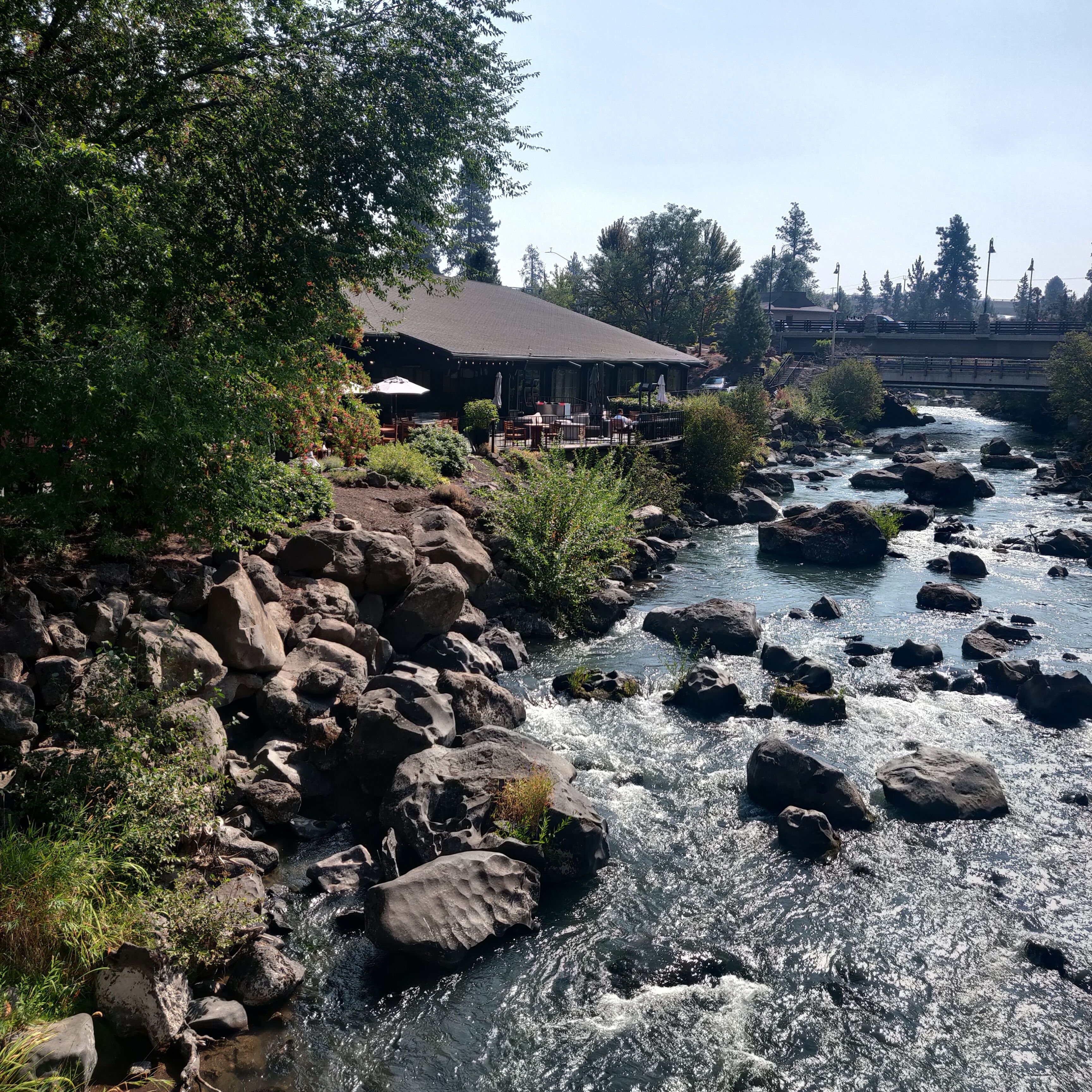 A riverside restaurant with outdoor seating, surrounded by rocks and greenery.