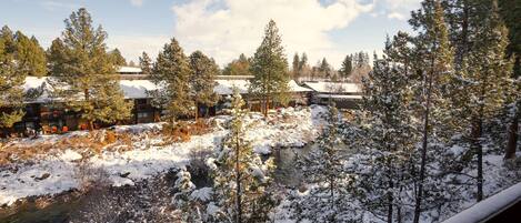 A snow-covered landscape with a river, trees, and buildings with snow on their roofs.