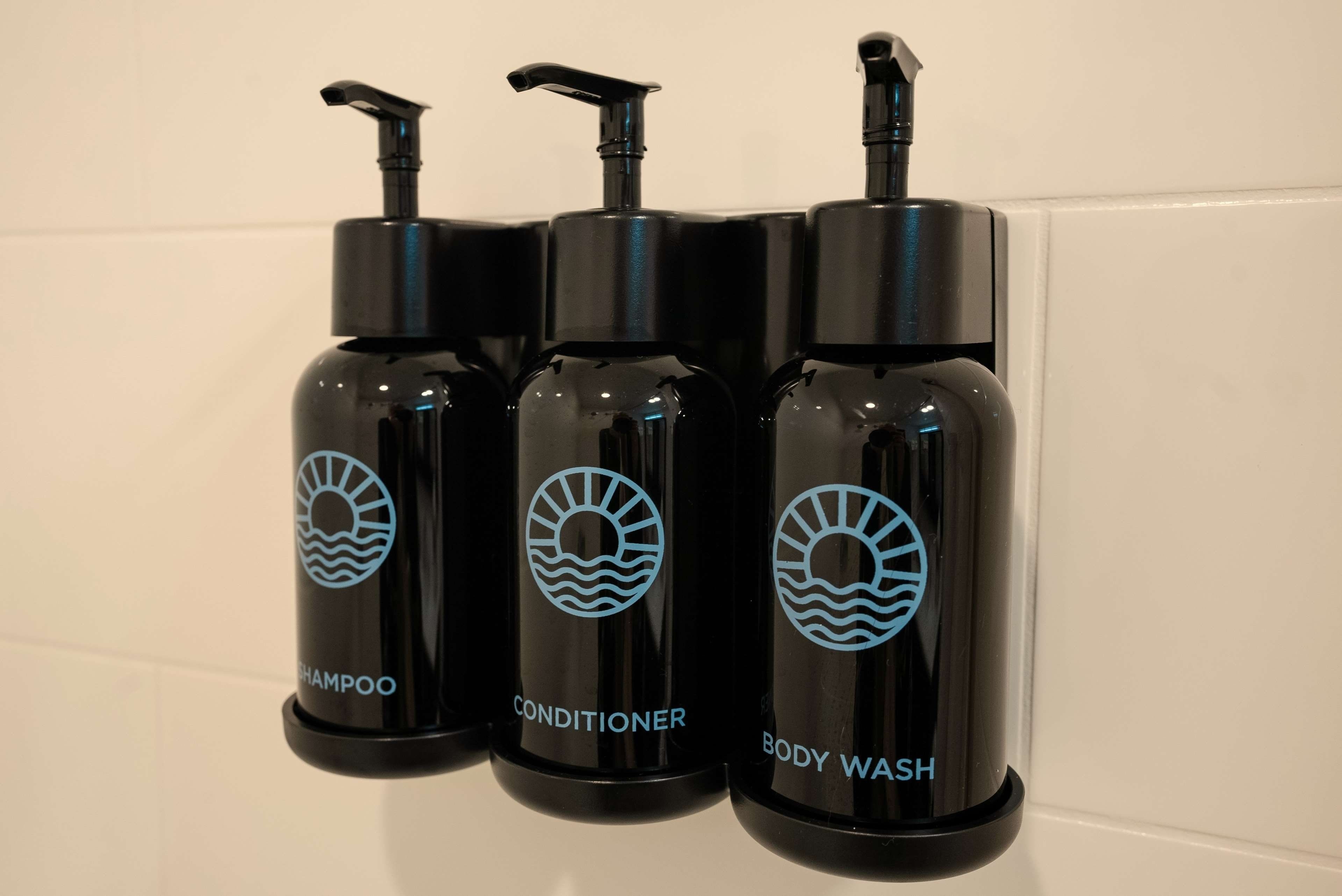 Three black bottles with pump dispensers, labeled 'SHAMPOO,' 'CONDITIONER,' and 'BODY WASH.'