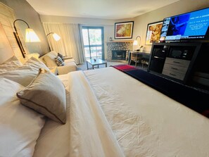Una habitación de hotel con una cama grande, televisión, chimenea y zona de comedor.