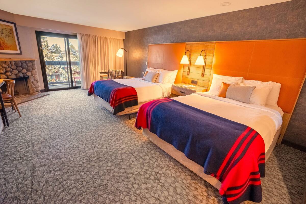 A hotel room with two beds, a fireplace, a balcony with a view, and a stone wall.