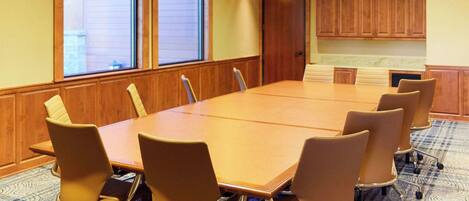 A conference room with a large table, chairs, a projector, and a view through the windows.