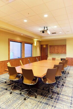 A conference room with a large table, chairs, a projector, and a view through the windows. - Riverhouse Lodge (Bend)