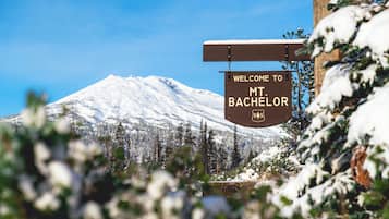 A sign welcoming visitors to Mt Bachelor with a backdrop of a snow-covered mountain and evergreen trees.